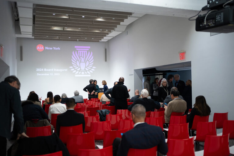 People are scattered throughout rows of red chairs inside the Tafel room at the Center for Architecture. A presentation at the front of the room displays the AIANY logo and the text "2024 Board Inaugural."