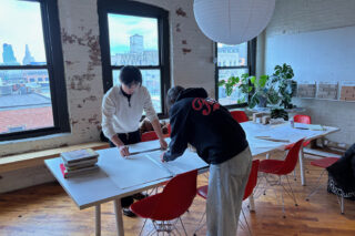 Two students standing, working over a table.