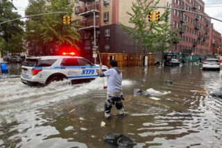 Image of a person walking in a flooded area while an NYPD car drives by.